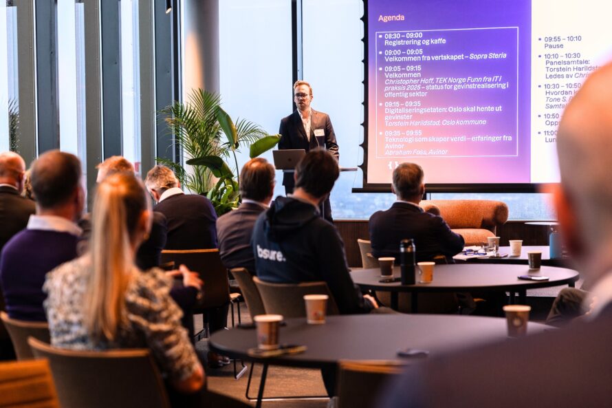 Christopher Hoff står ved siden av presentasjonsskjermen i 26. etg hos Sopra Steria. Bilde av deltakere i forgrunnen.