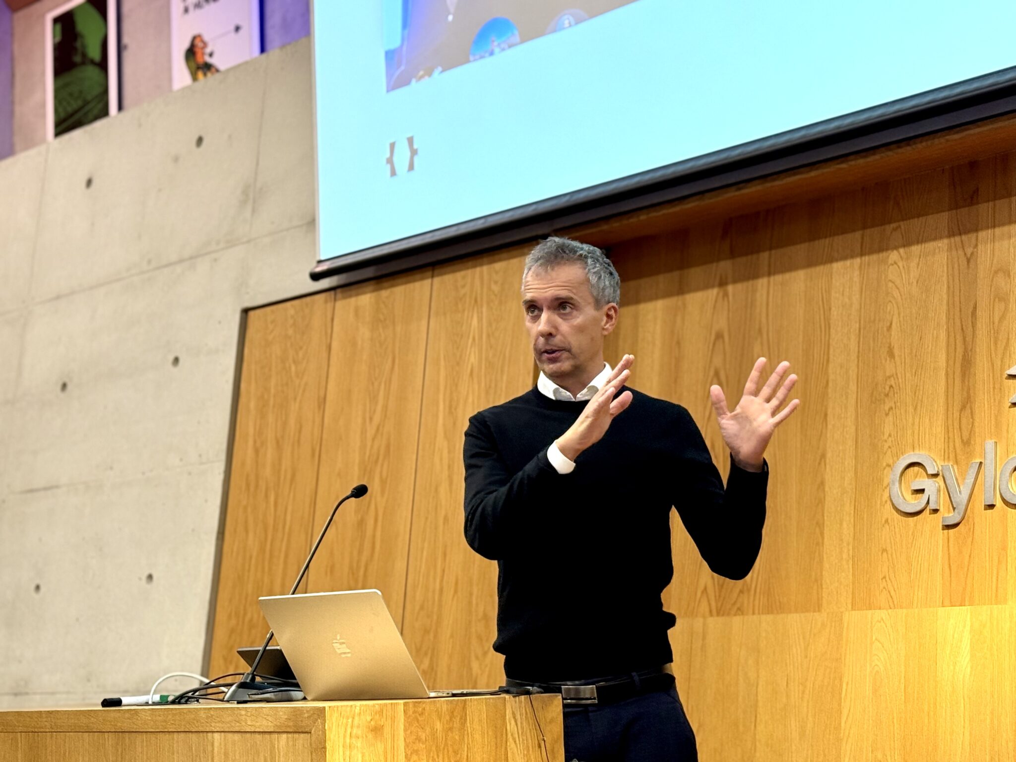 Jarle Roheim Håkonsen står foran podiet hos Gyldendal, med pc og gestikulerer entusiastisk med hendene.