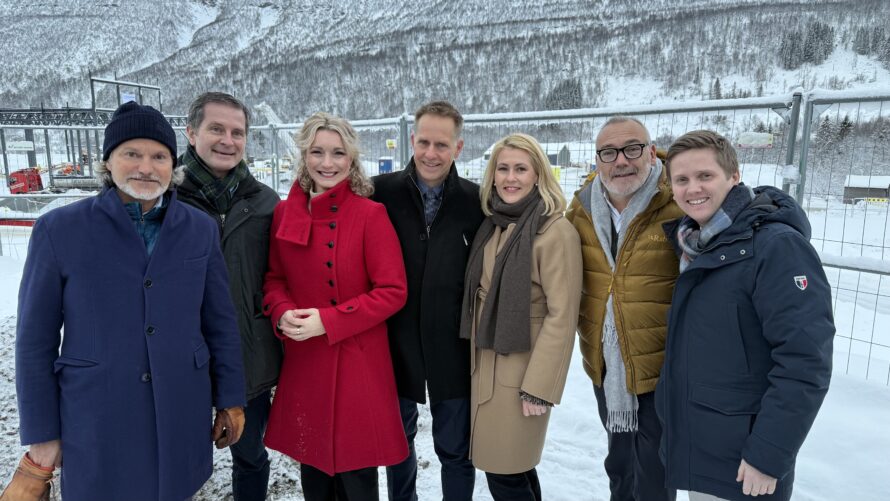 Bilde av en gruppe mennesker i vinterklær foran fjell på byggeplass